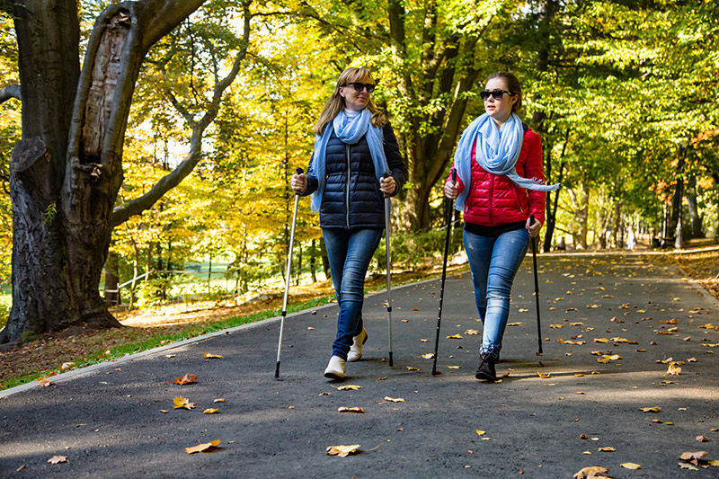 Two women walking thru the city park with hiking poles